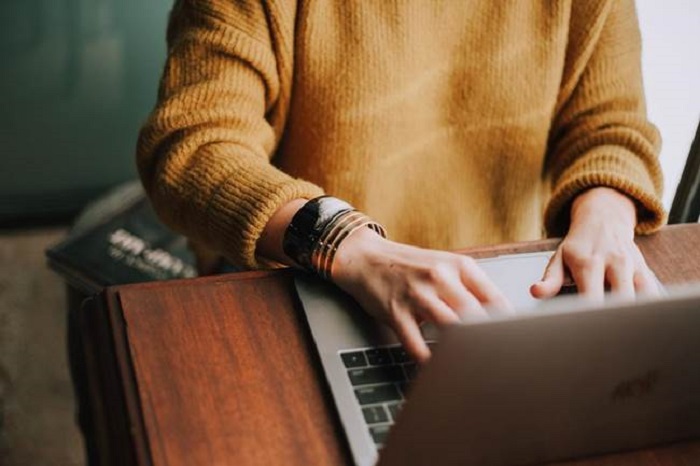 A professional working on a laptop wearing a cozy mustard sweater, implementing professional service automation to help streamline and optimize business operations.